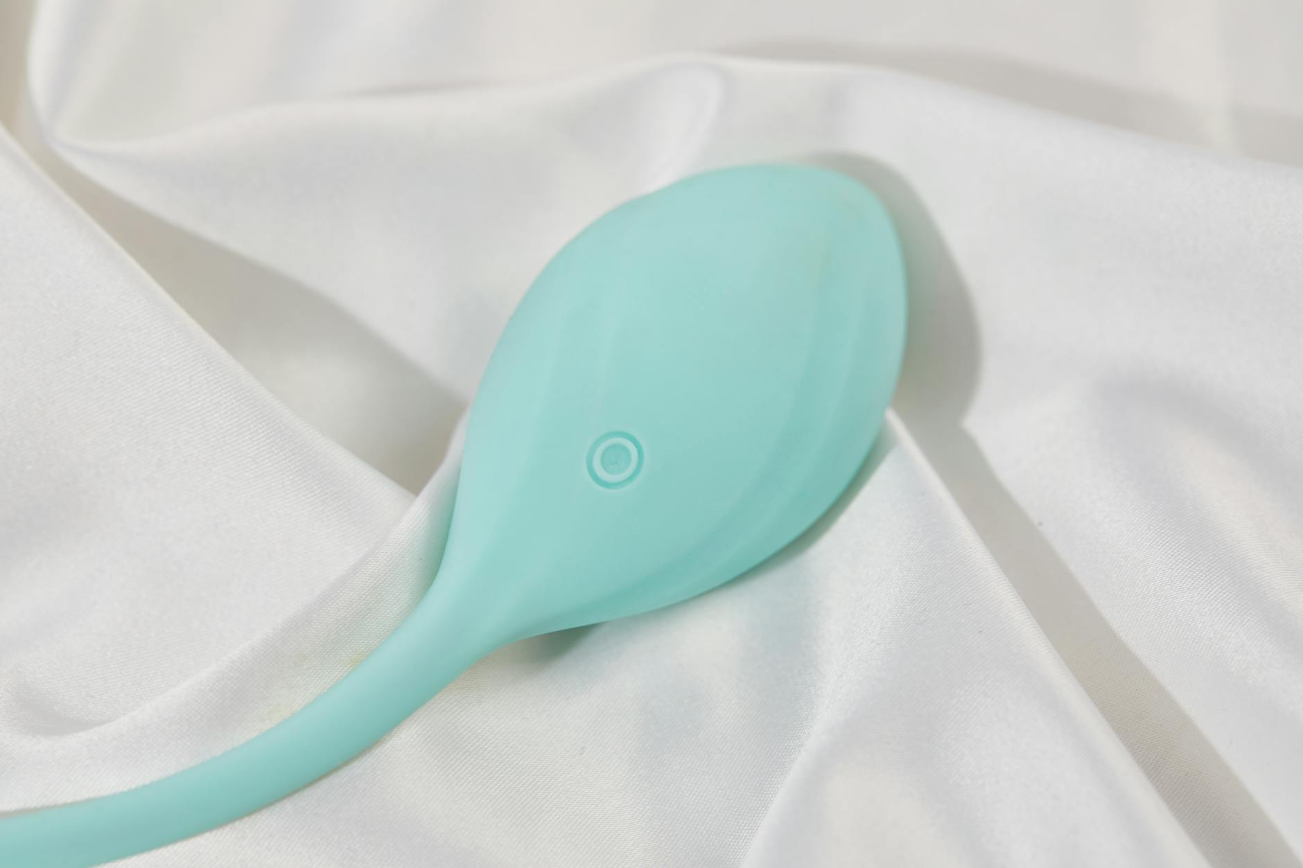 A sleek teal lemon vibrator on soft white silk fabric