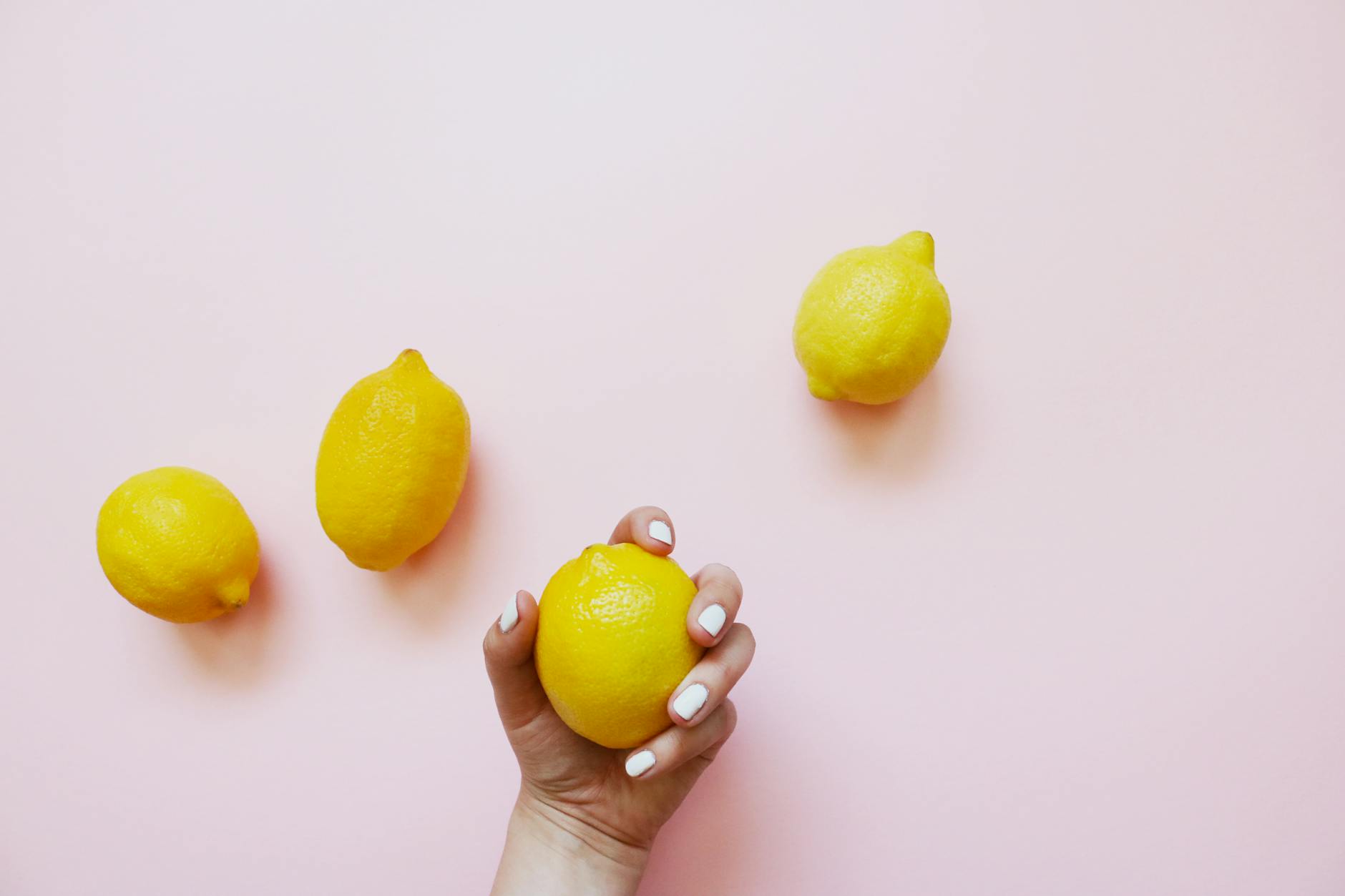 Warm hand holding bright lemon on soft pink background, symbolizing gentle postpartum recovery and self-care