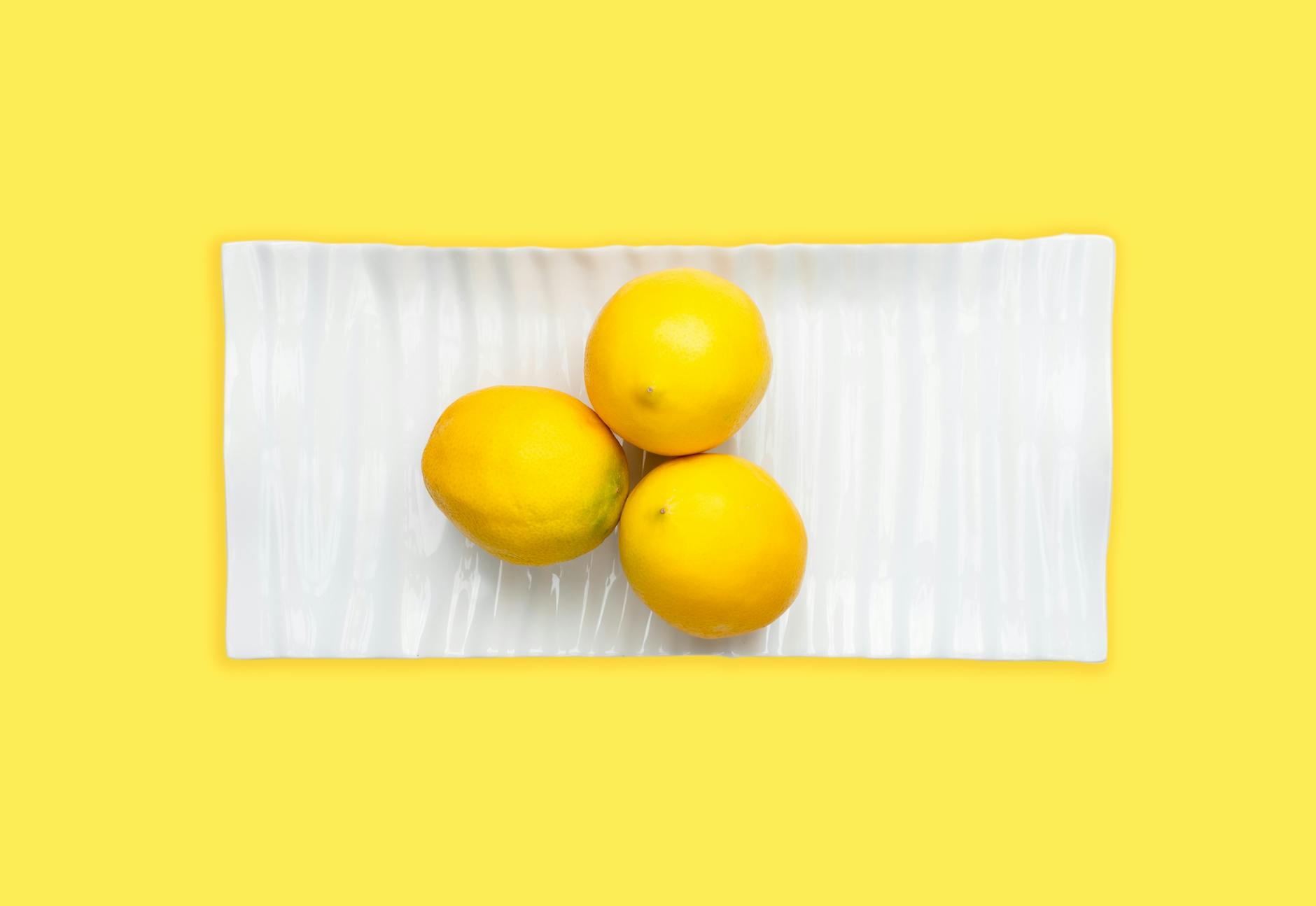 Three fresh lemons arranged on a white plate, symbolizing the simplicity and joy of introducing new pleasure tools to couples intimacy.