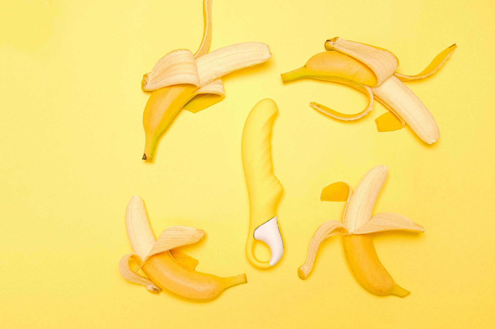 Colorful vibrator surrounded by flowers and citrus on yellow background