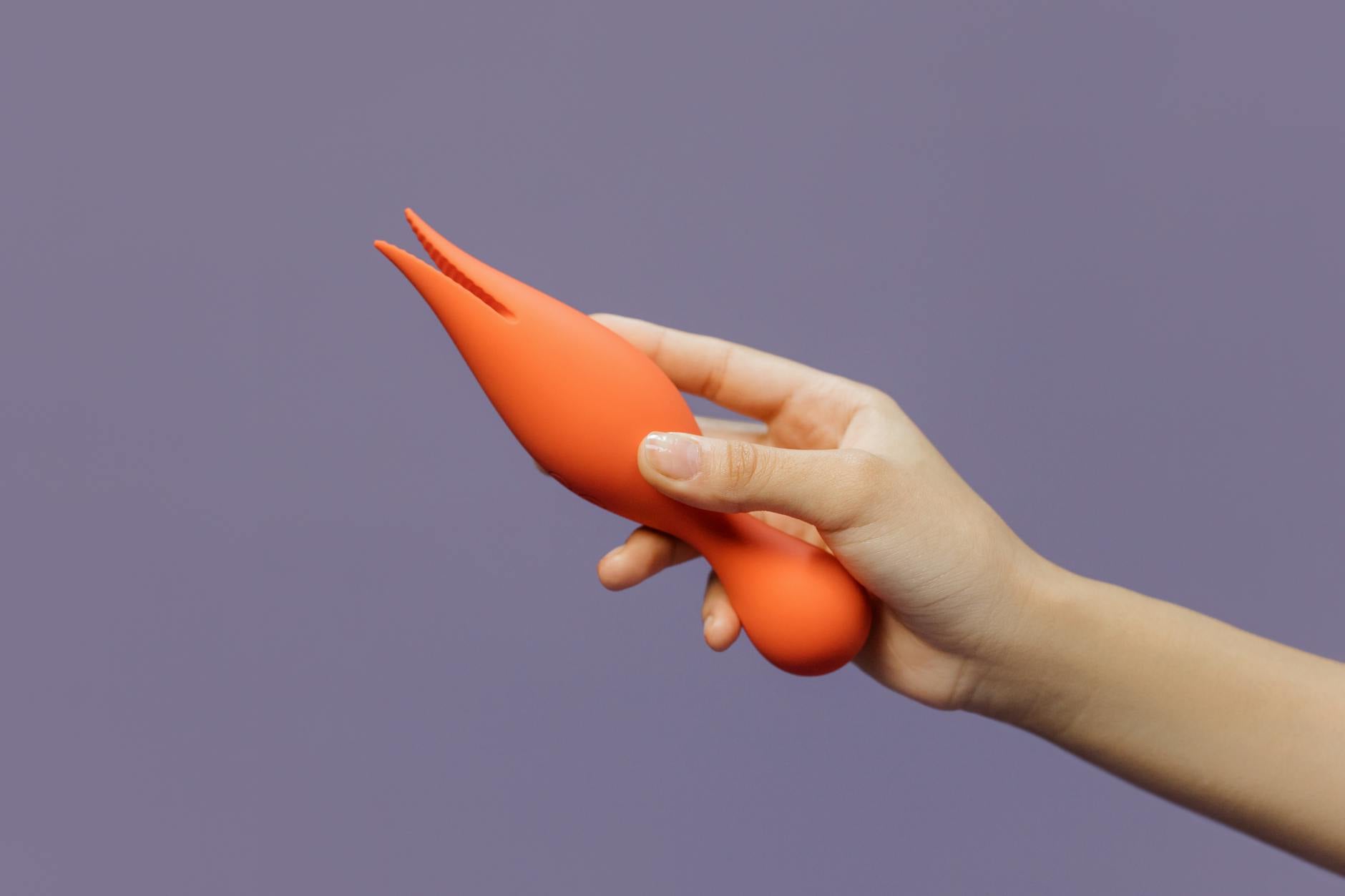 A blue silicone vibrator held in hand against a minimalistic purple backdrop