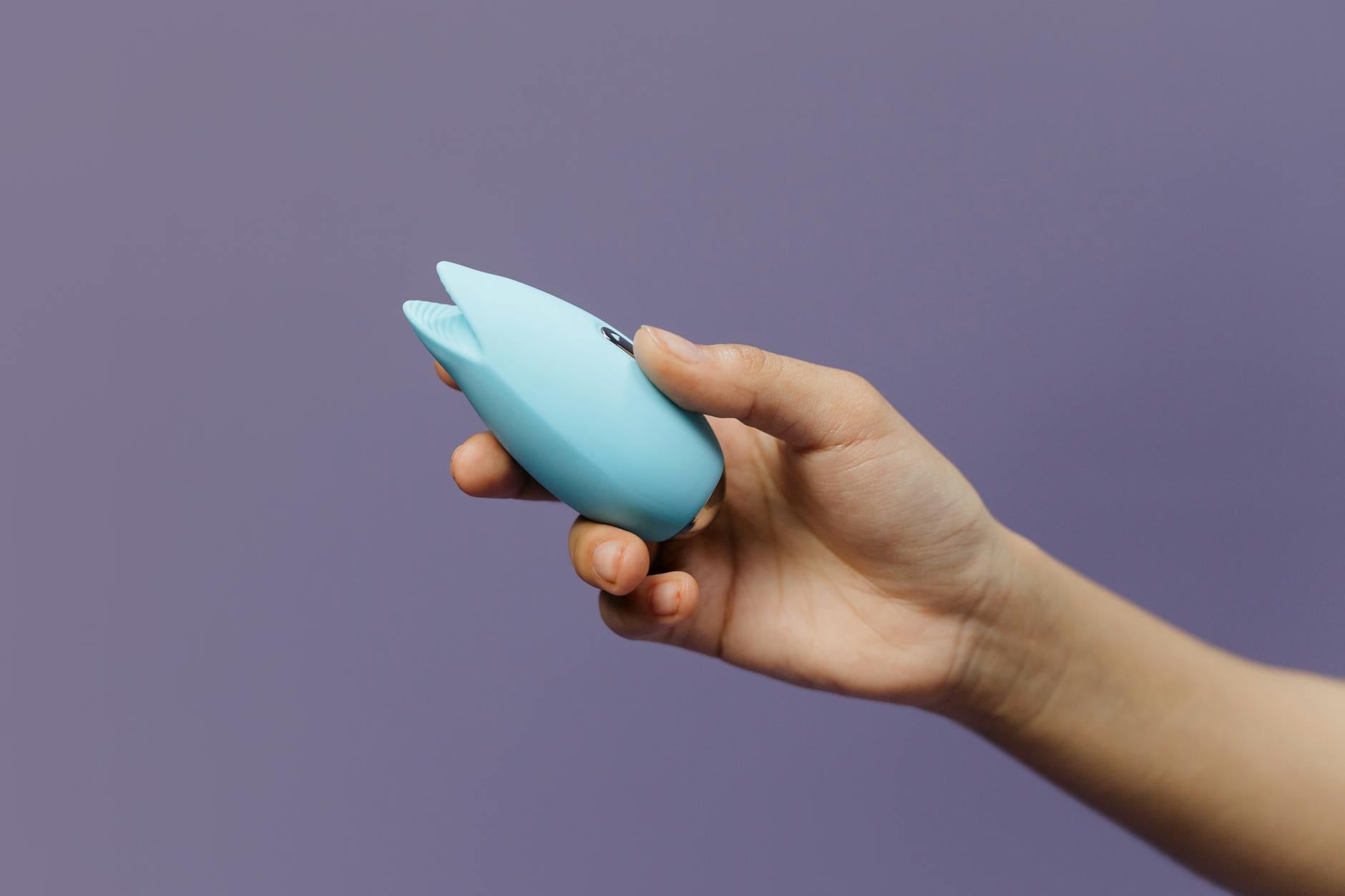 A blue silicone clitoral vibrator held gently in hand, symbolizing safe exploration and self-compassion