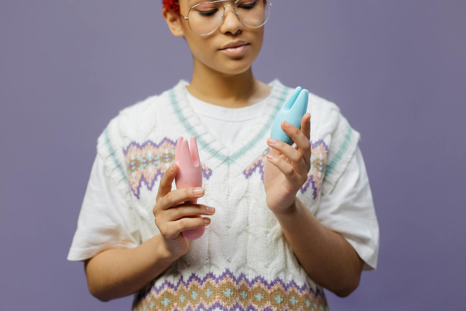Blue silicone clitoral vibrator held in hand against purple background